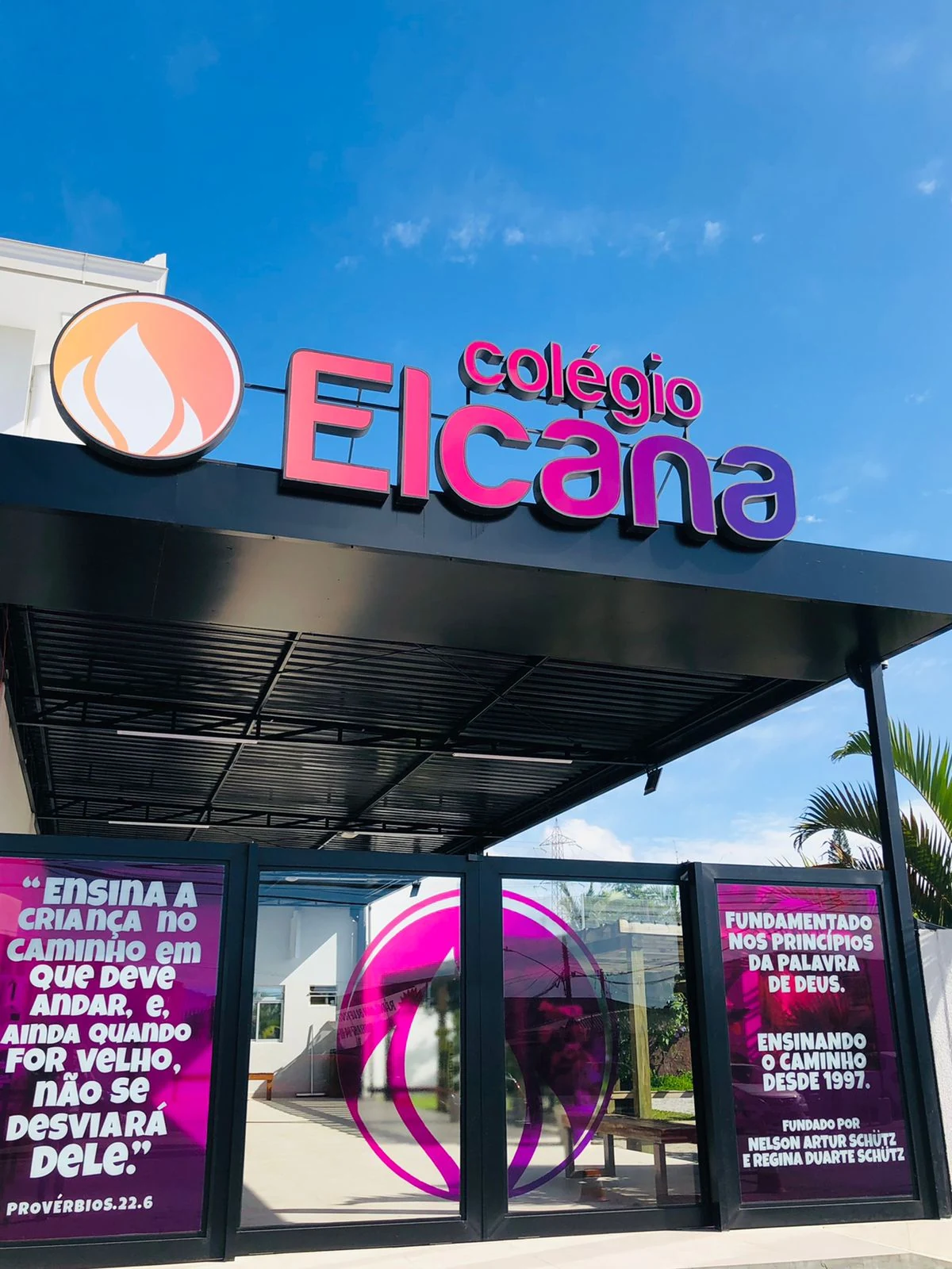 Identificação do Colégio Elcana sobre a fachada azul do estabelecimento.
