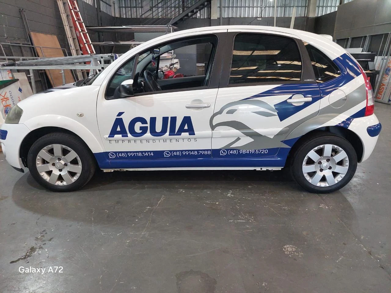 Veículo da Águia Empreendimentos com aplicação gráfica azul, branca e prata, visto de lado.