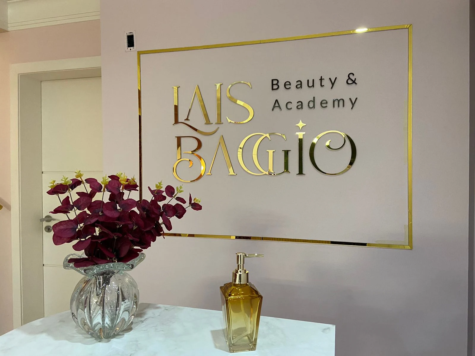 Letreiro dourado Laís Baggio Beauty & Academy instalado na parede de uma recepção.