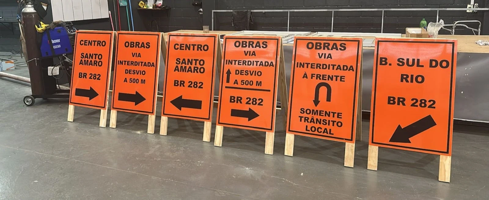 Conjunto de placas laranja de sinalização de obras fotografado no galpão.